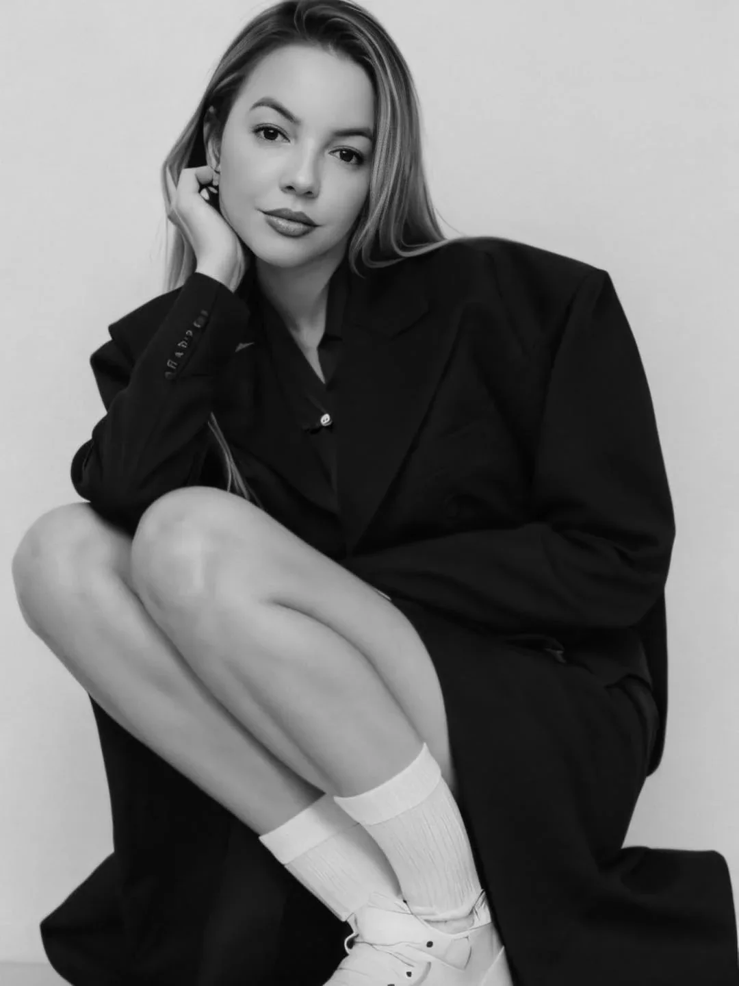 Roberta Graciana agachada, de blazer oversized preto e meias brancas, em foto preto e branco