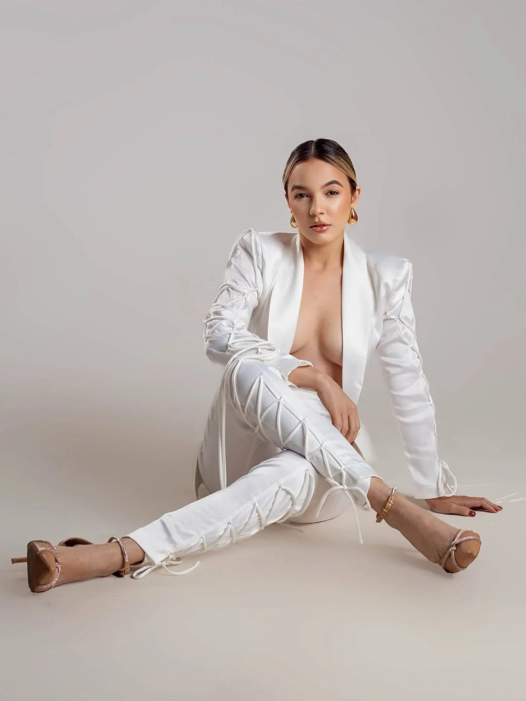 Roberta Graciana sentada no chão, de terno branco com amarrações e sandálias nude